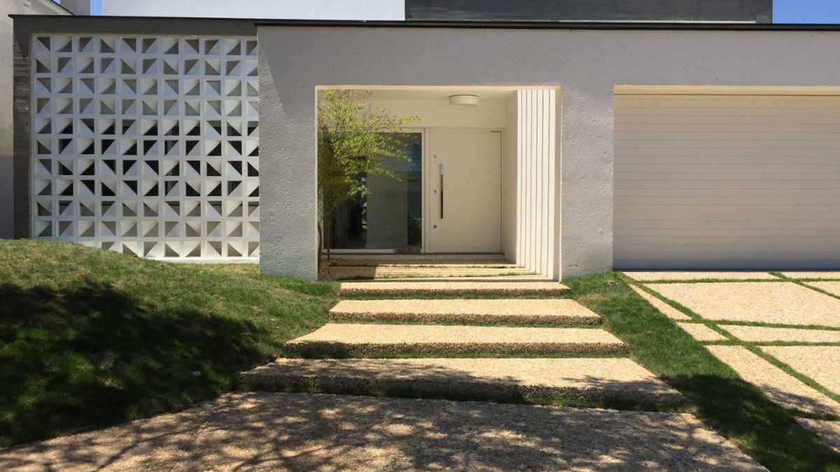 Fachada comercial de consultório decorada com cobogó branco, grama e pisantes de concreto.