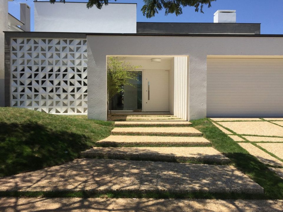 Fachada comercial de consultório decorada com cobogó branco, grama e pisantes de concreto.